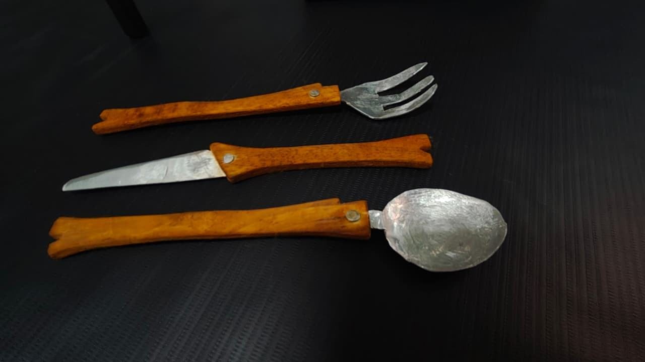 Knife, fork and spoon with orange handles on a dark surface