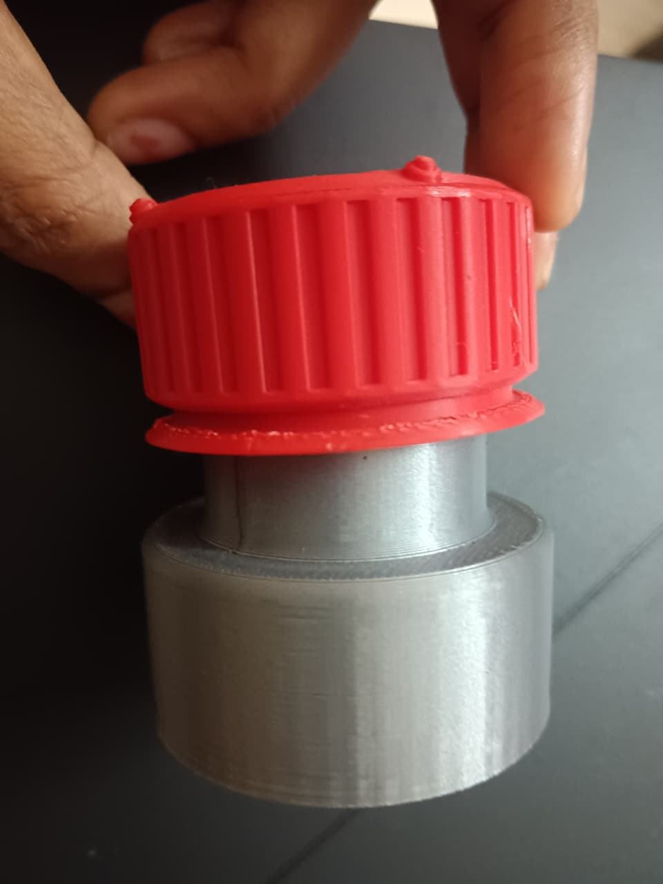 A hand turning the red cap on the silver body