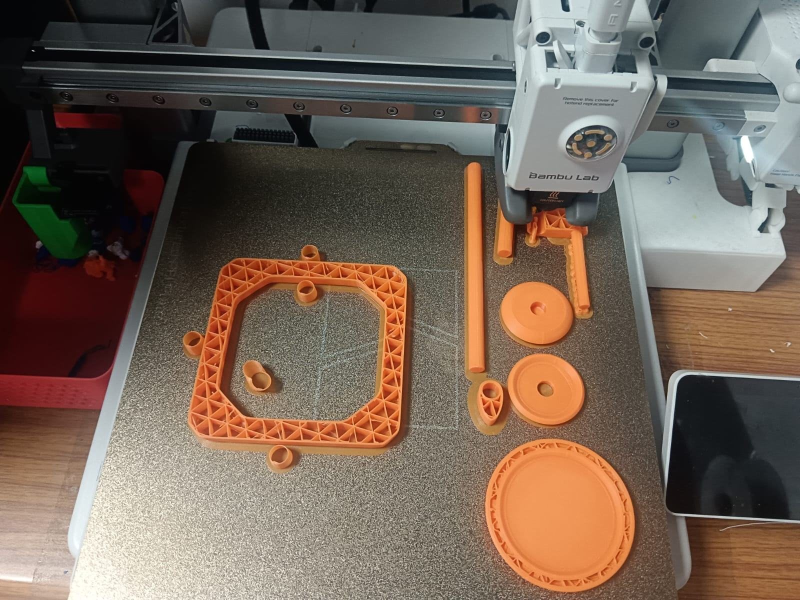 Printed orange frame, gears and handle parts on the print bed